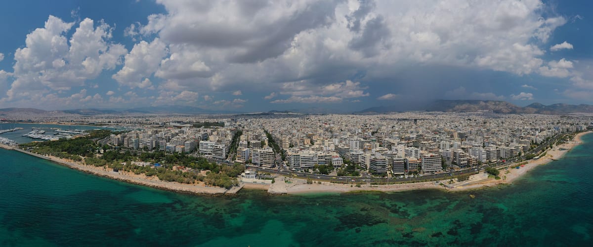An aerial view of a coastal city with a dense urban area, a beach, and clear blue waters.