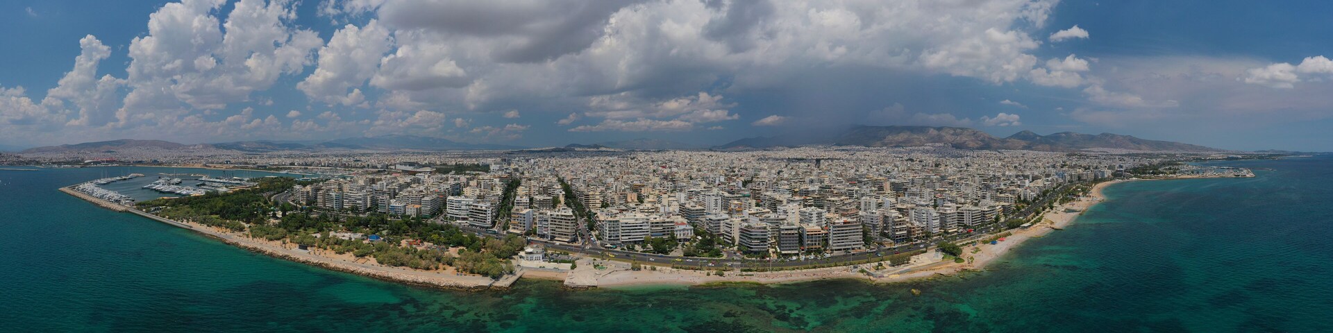An aerial view of a coastal city with a dense urban area, a beach, and clear blue waters.