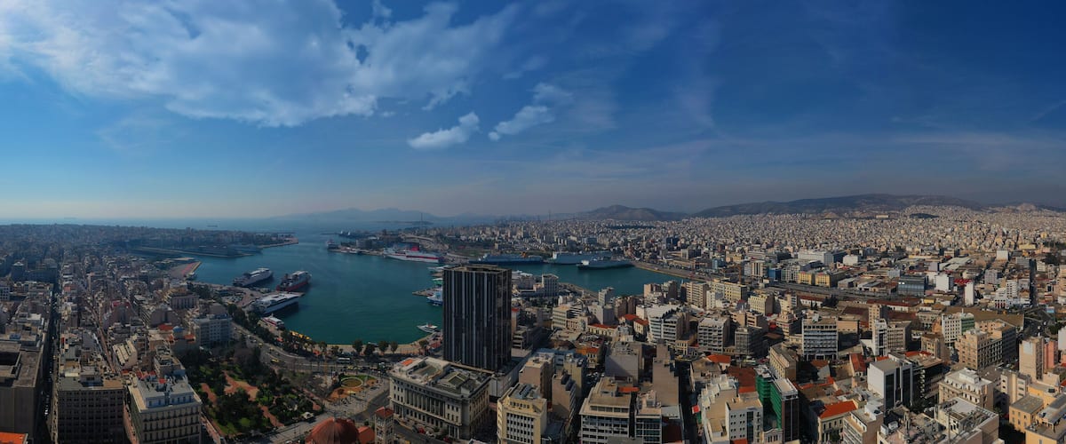 A coastal cityscape with a harbor, dense urban buildings, and distant mountains.