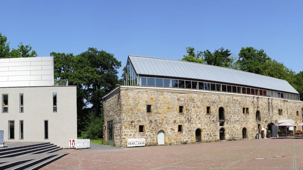 A museum with red umbrellas, a modern building, a stone structure, and a historic red building with a tower.