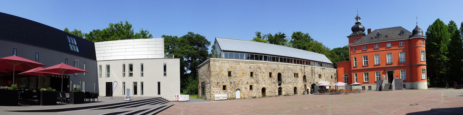 A museum with red umbrellas, a modern building, a stone structure, and a historic red building with a tower.