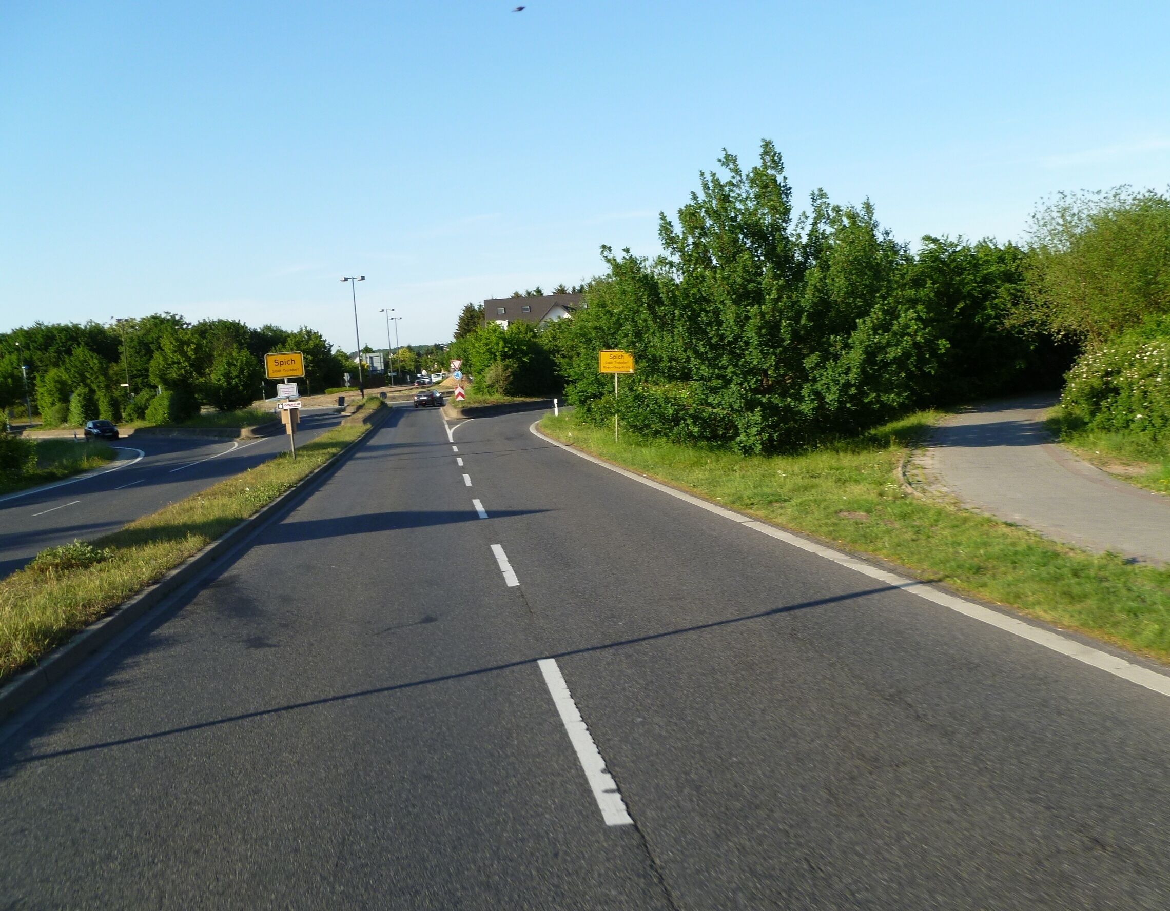 A two-lane road with a curve, surrounded by greenery and trees.