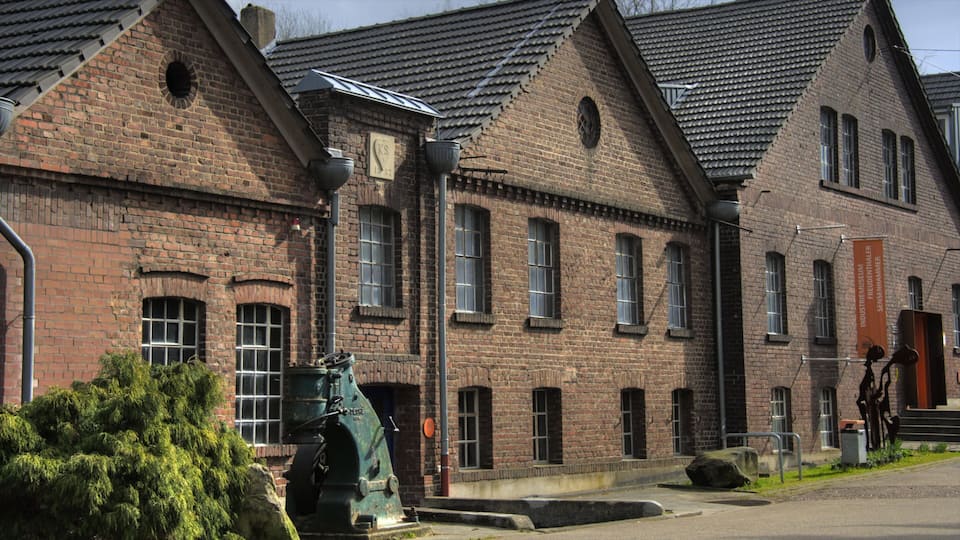 Un bâtiment historique en briques, doté de grandes fenêtres, avec une machine verte en premier plan.