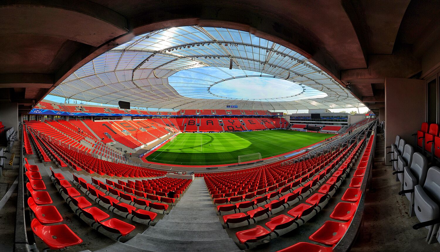 A large, empty stadium with red seats and a green field.