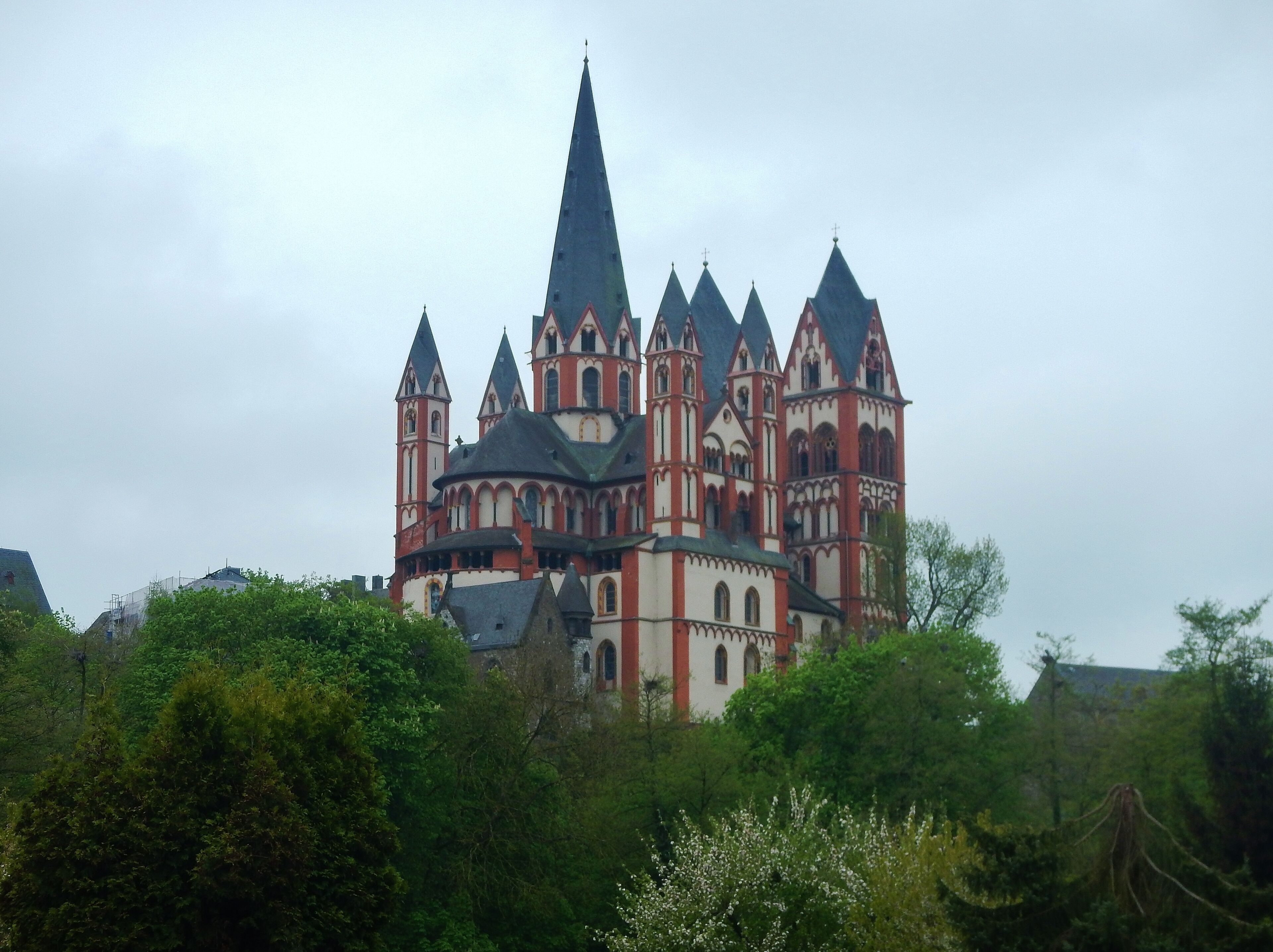 A large, historic building with multiple spires and towers, surrounded by lush greenery.
