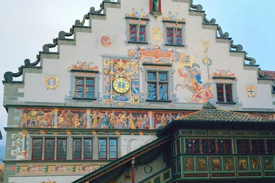Un edificio con murales ornamentales, un reloj y una escalera que conduce a una entrada.