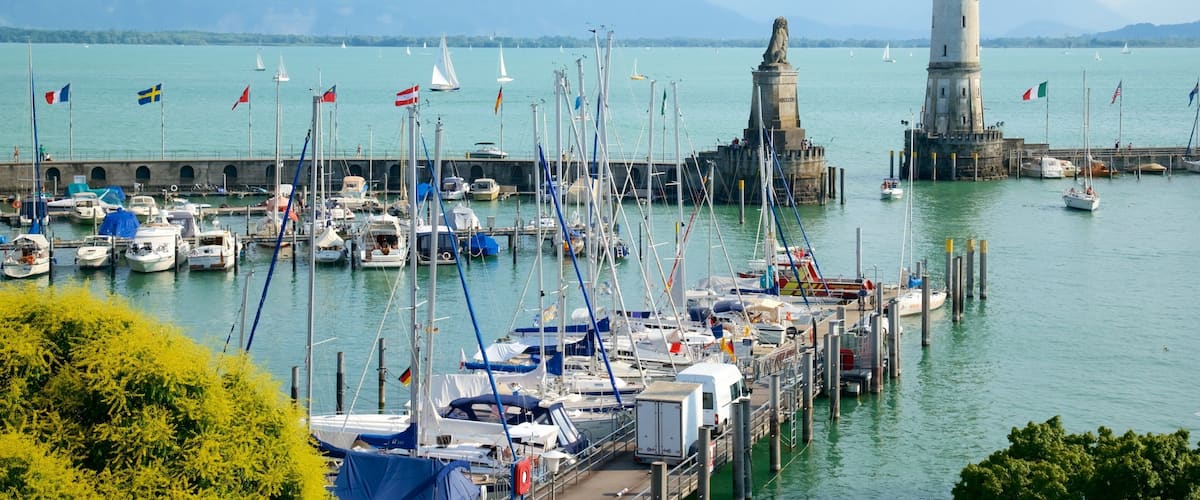 A harbor with boats, a lighthouse, and mountains in the background.