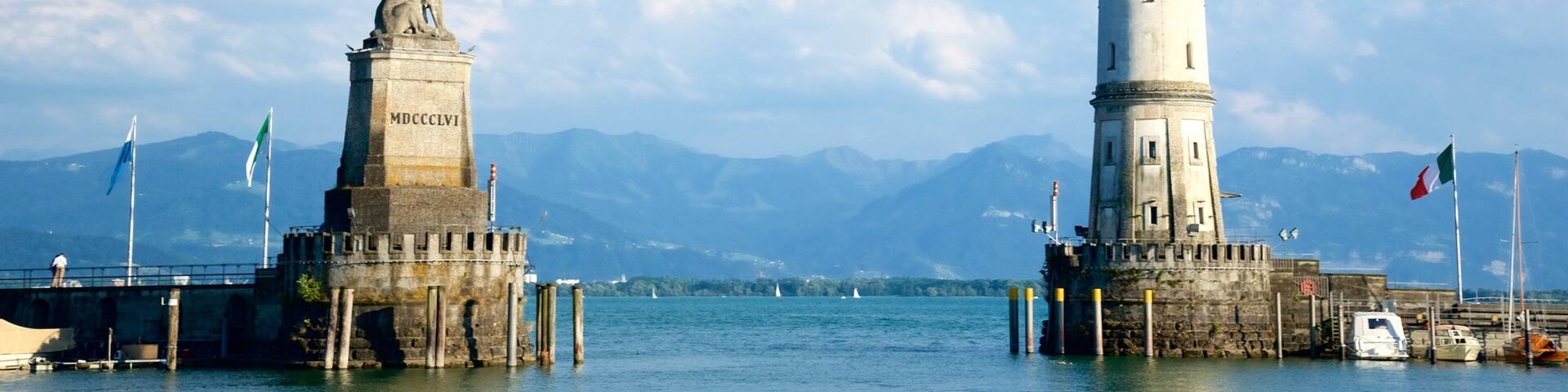 A lighthouse and a statue on a pier with mountains in the background.