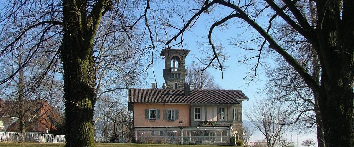A historic building with a tower, surrounded by trees and a grassy area.