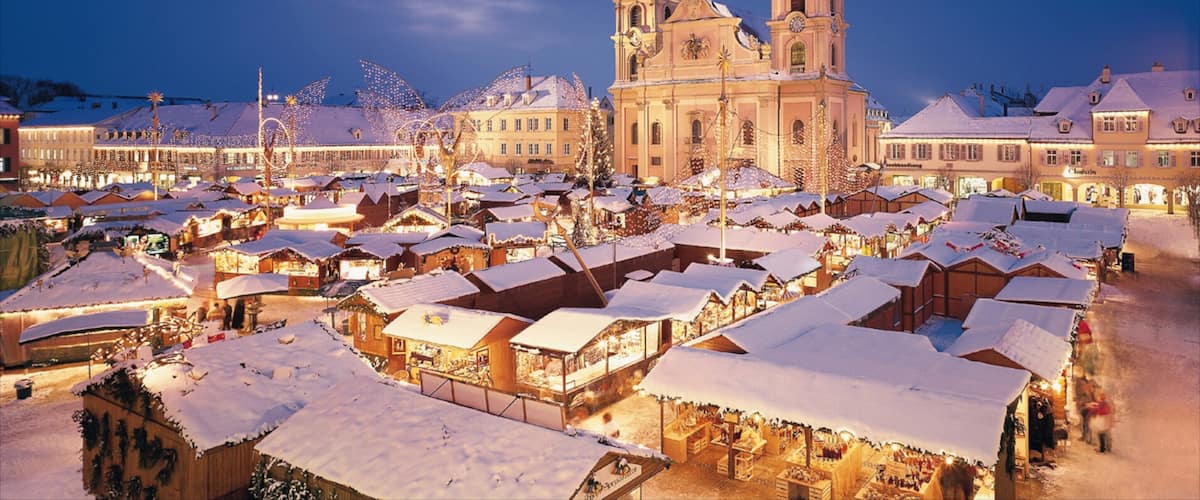 A snow-covered market square with historic buildings and a prominent church with two towers.