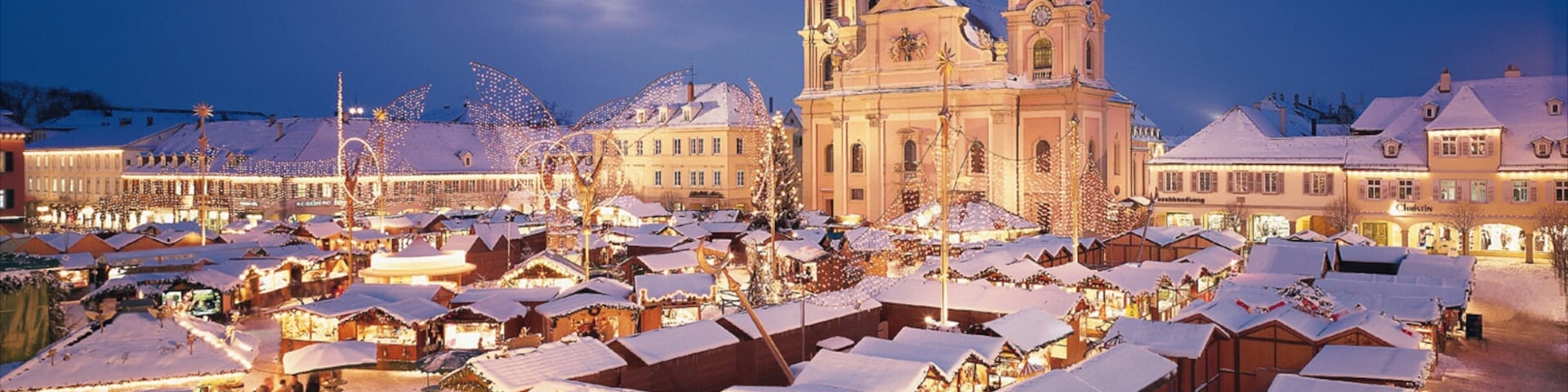A snow-covered market square with historic buildings and a prominent church with two towers.