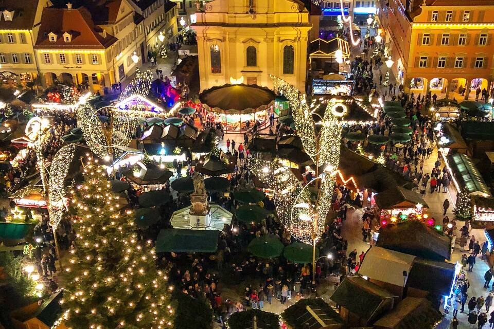 A festive market square with illuminated trees, a prominent church, and traditional market stalls.