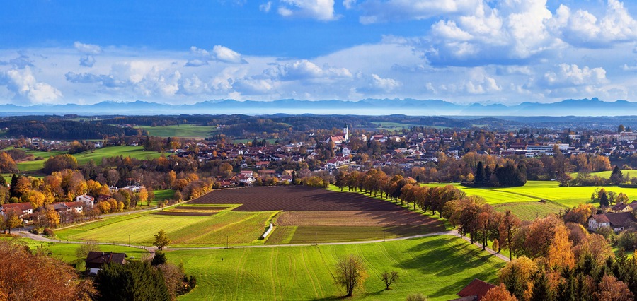 A town with a prominent church, surrounded by fields and autumn-colored trees.