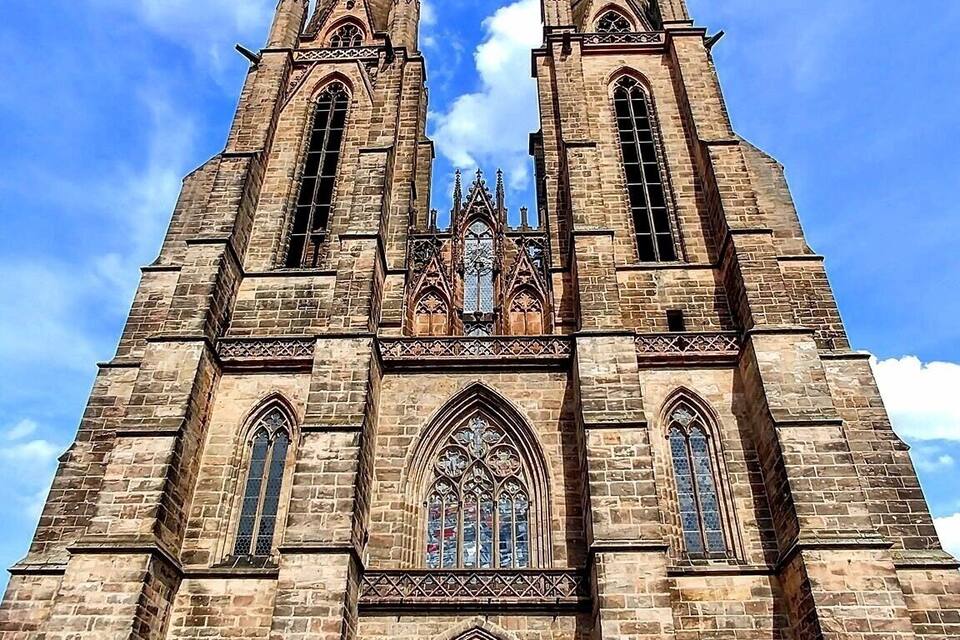 Une vaste église de style gothique, dotée de deux flèches jumelles et de motifs complexes dans ses vitraux.