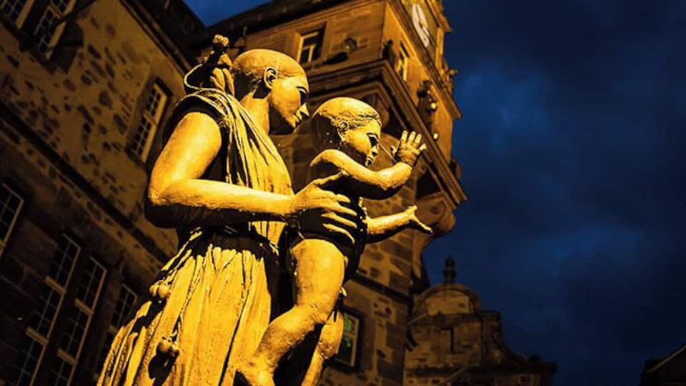 Eine Statue einer Frau, die ein Kind hält, vor einem historischen Gebäude mit einem Glockenturm.