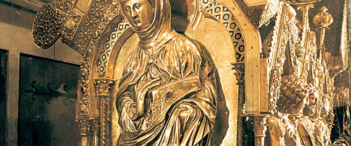 A golden statue of a robed figure with intricate architectural details in the background.