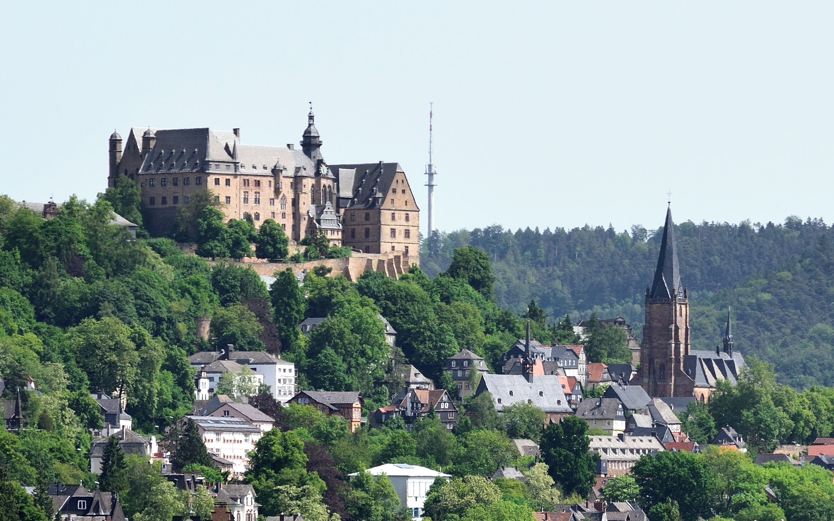A historic castle on a hill with a church spire in the foreground.