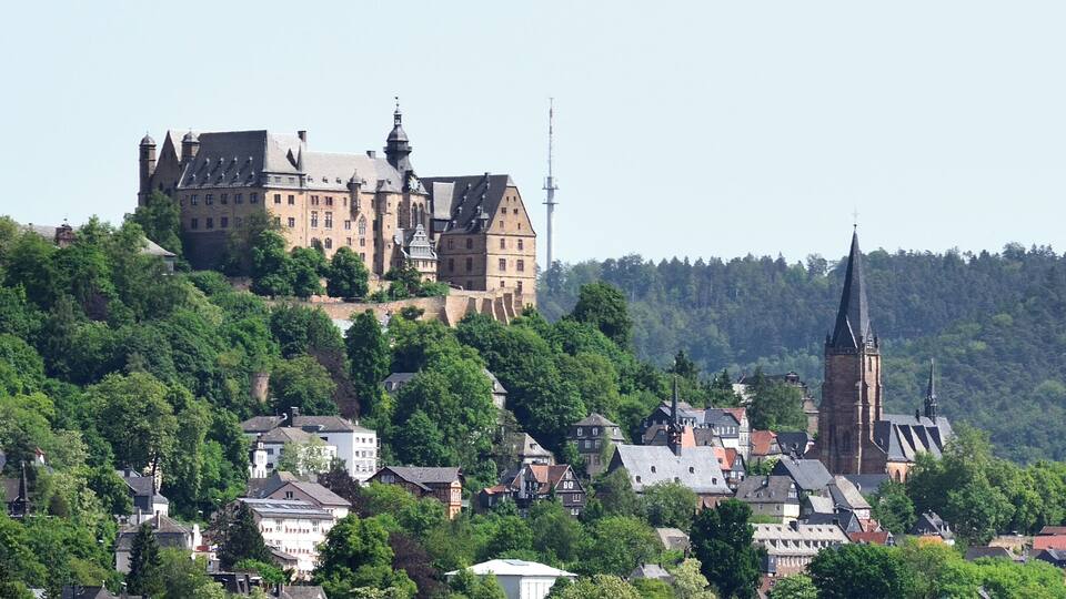 A historic castle on a hill with a church spire in the foreground.