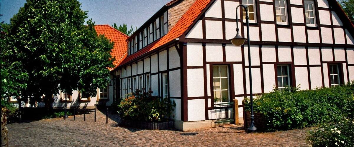 A traditional half-timbered house with a red-tiled roof, surrounded by cobblestone paths and greenery.