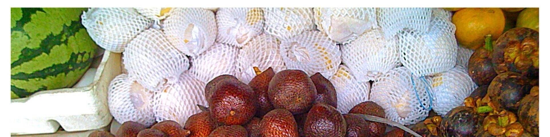 A market stall with a variety of fruits, including round, brownish items and some with green tops.