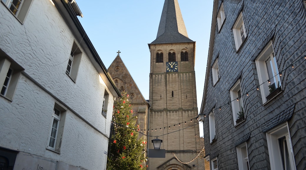 A narrow street with a church tower featuring a clock, surrounded by buildings with textured facades.