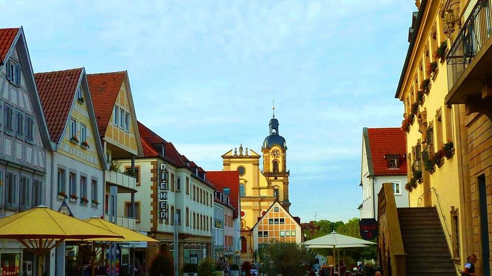 A European town square with historic buildings, a church with a clock tower, and outdoor seating areas.
