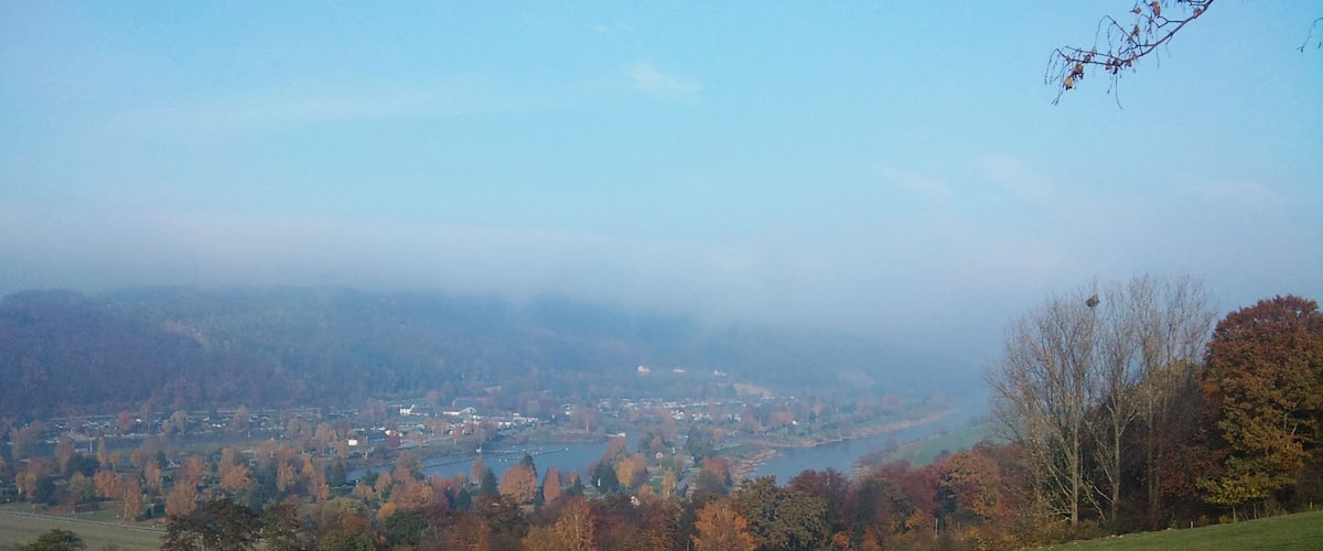 A panoramic view of a valley with a river, autumn-colored trees, and a distant town.