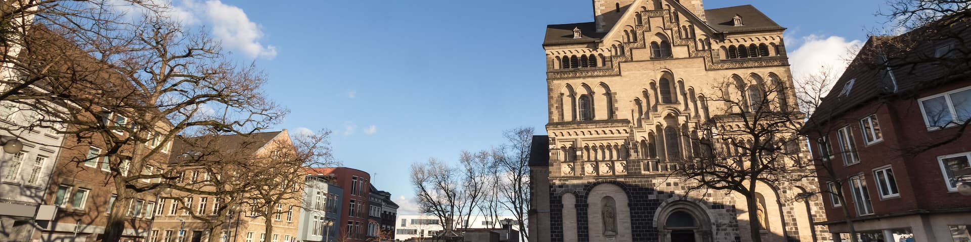 A historic church with a tall tower, surrounded by urban buildings and leafless trees.