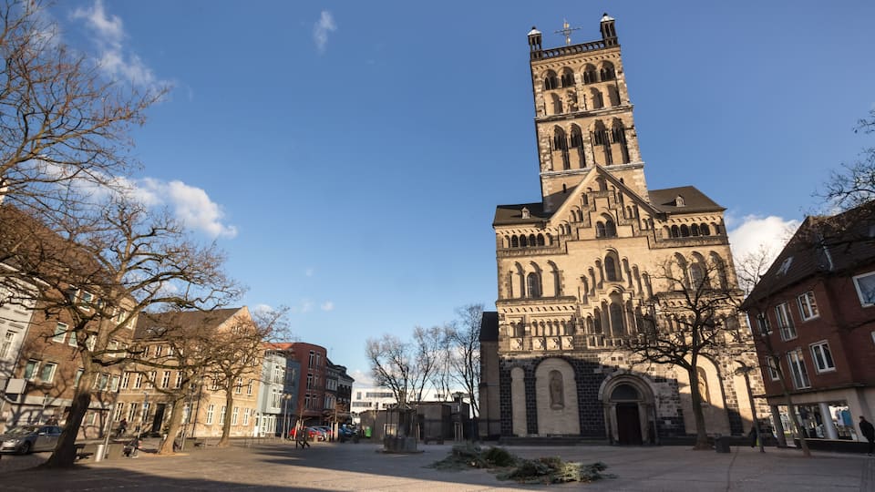 A historic church with a tall tower, surrounded by urban buildings and leafless trees.