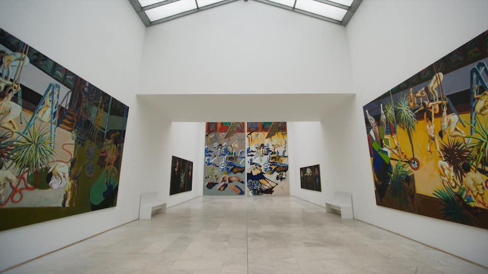 Una galería de arte con pinturas grandes en las paredes y un tragaluz arriba.