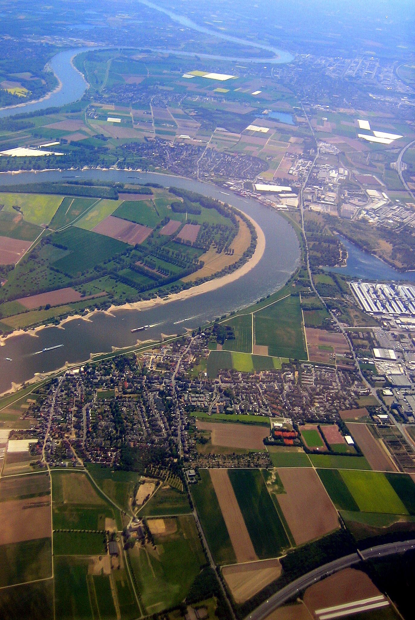 An aerial view of a river winding through a town with surrounding agricultural fields and industrial areas.