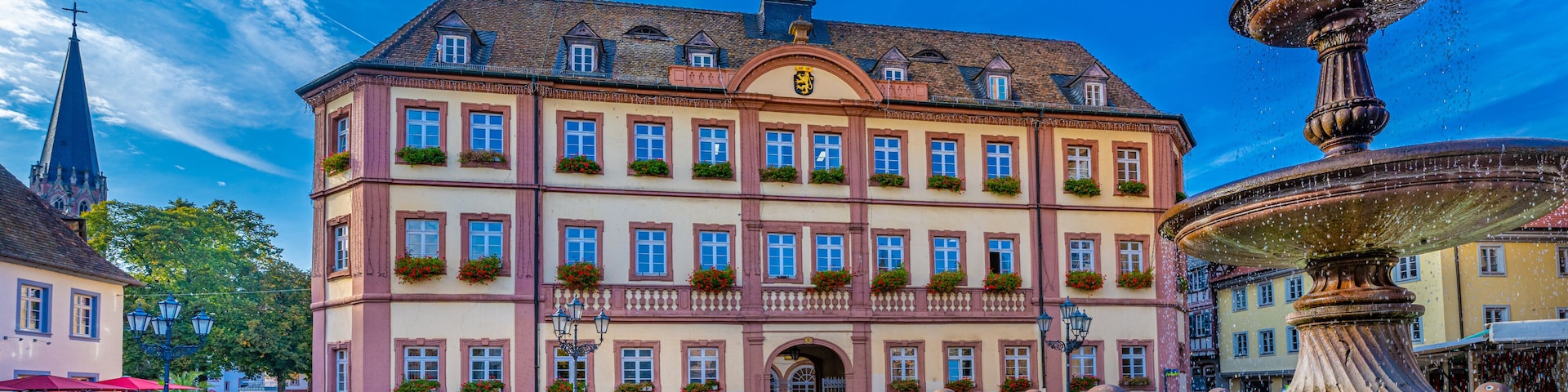 Un edificio histórico con una torre de reloj, una fuente y calles empedradas.