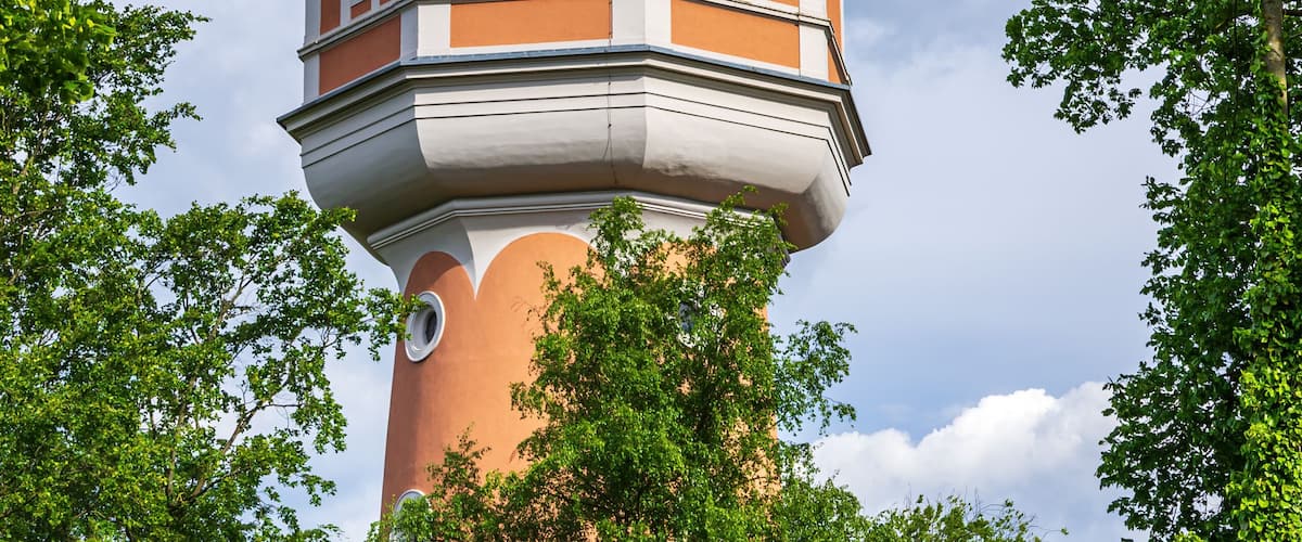 A tower with a dome and a spire, surrounded by lush green trees.
