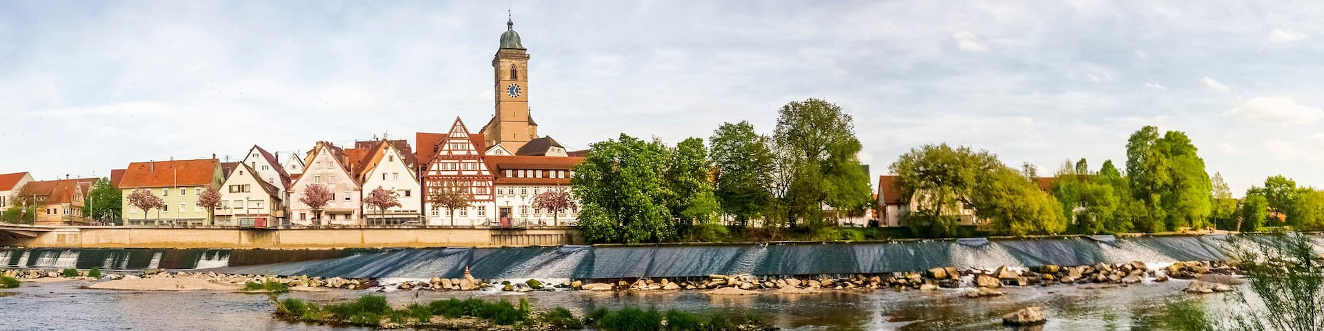 A river with a bridge, a clock tower, and traditional buildings along the riverbank.