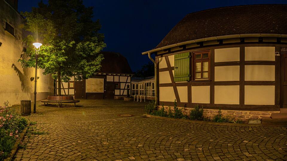 A cobblestone courtyard with traditional half-timbered houses, a bench, and a street lamp.