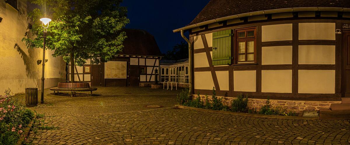 A cobblestone courtyard with traditional half-timbered houses, a bench, and a street lamp.