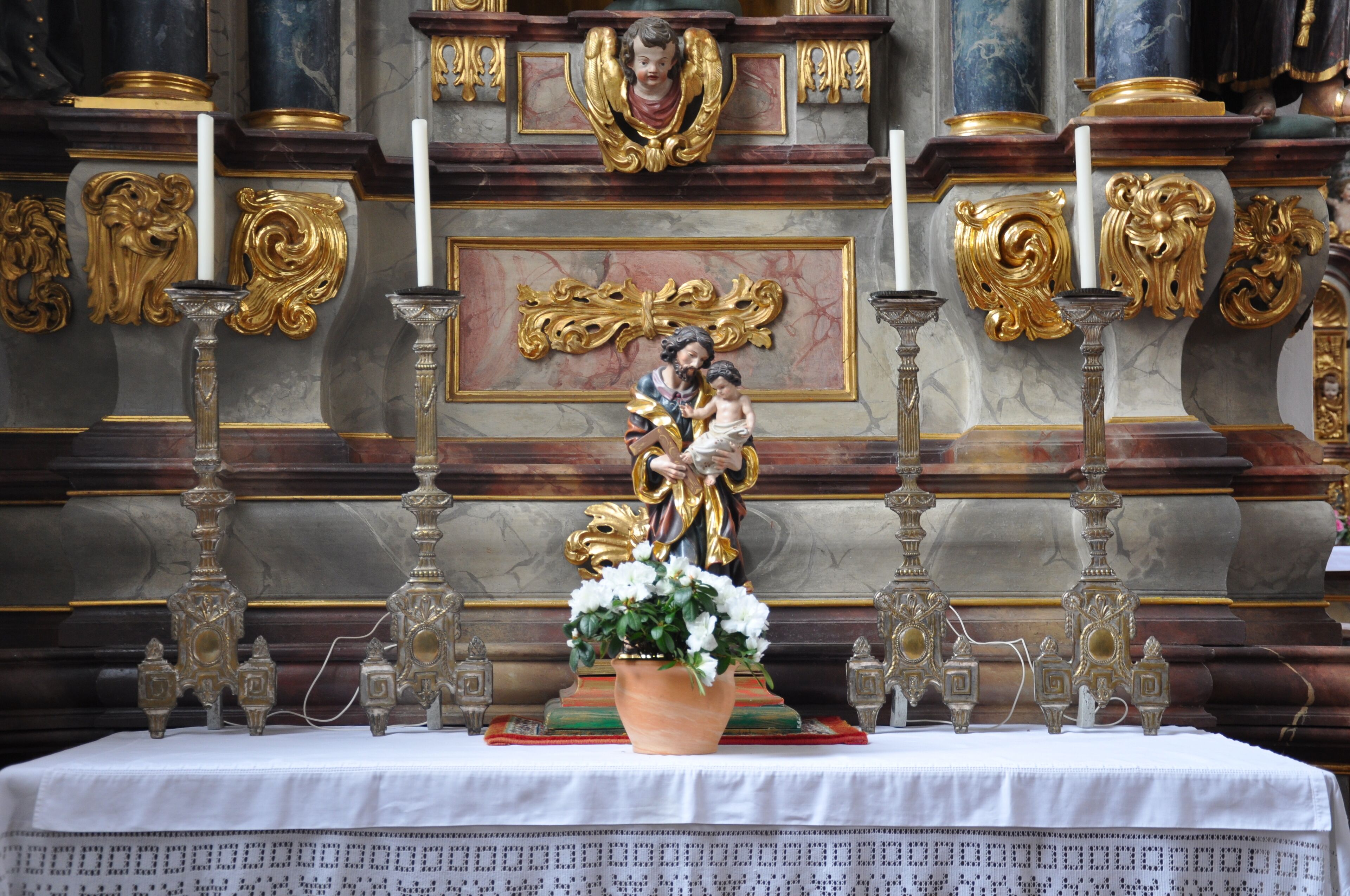 Wangen im Allgäu, Spitalkirche Heilig Geist, linker Seitenaltar, Mensa mit Figur "Hl. Josef mit Kind" und Altarleuchtern (Silberblech auf Holzkern, 18./19. Jh.)