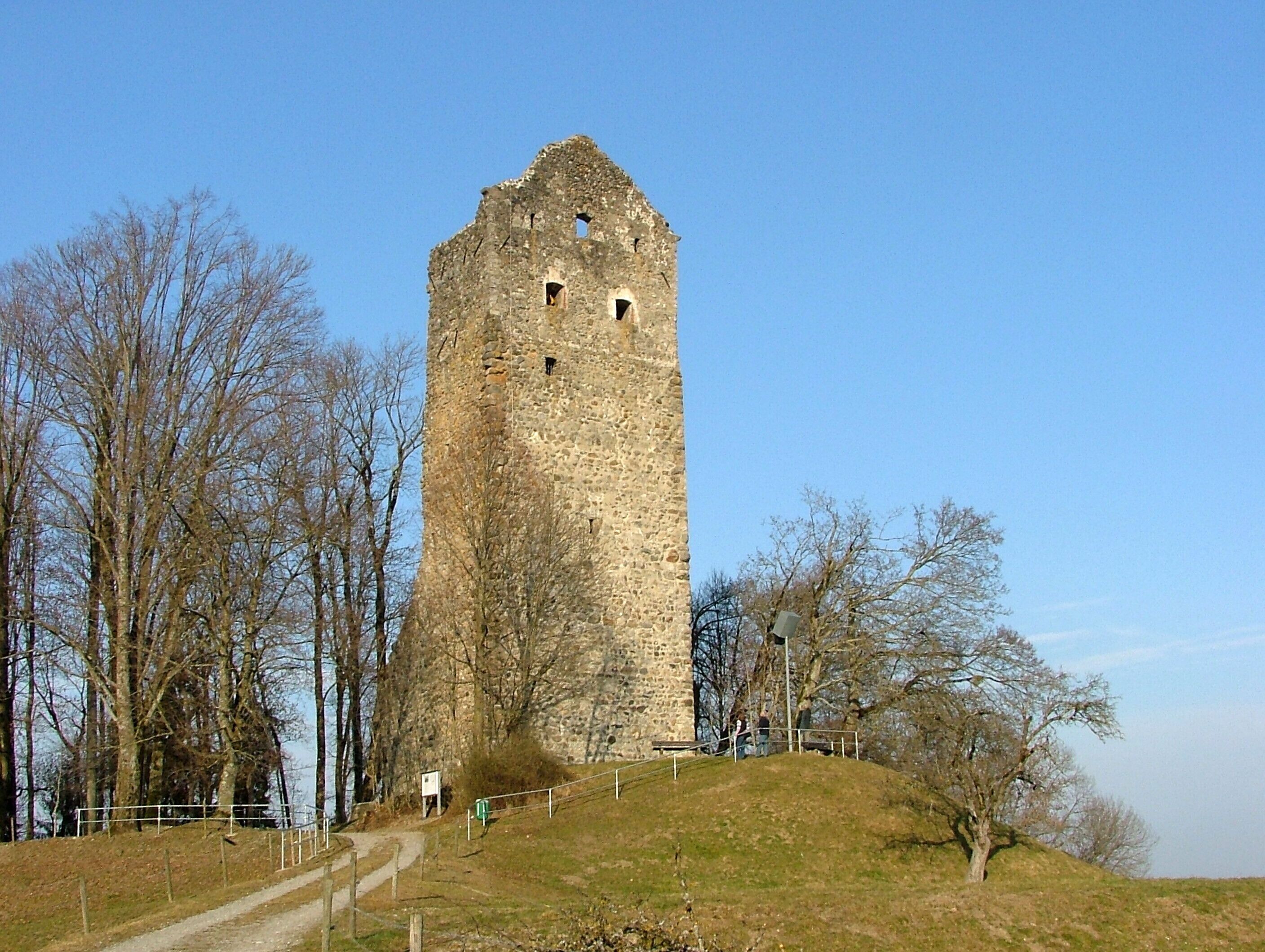 A tall stone tower with a steep, narrow staircase leading up to it, surrounded by leafless trees and a clear sky.