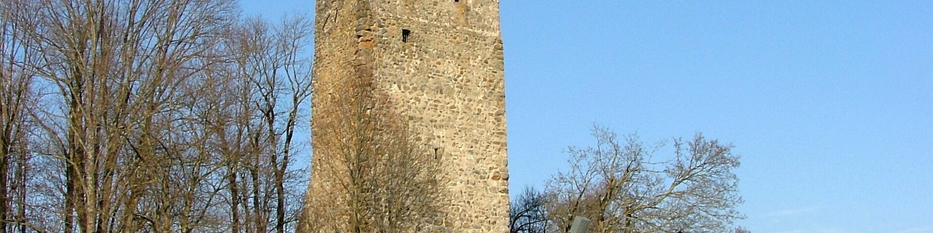 A tall stone tower with a steep, narrow staircase leading up to it, surrounded by leafless trees and a clear sky.