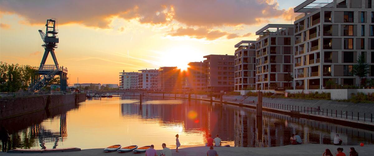 A sunset over a calm river with boats, a bridge, and modern buildings.