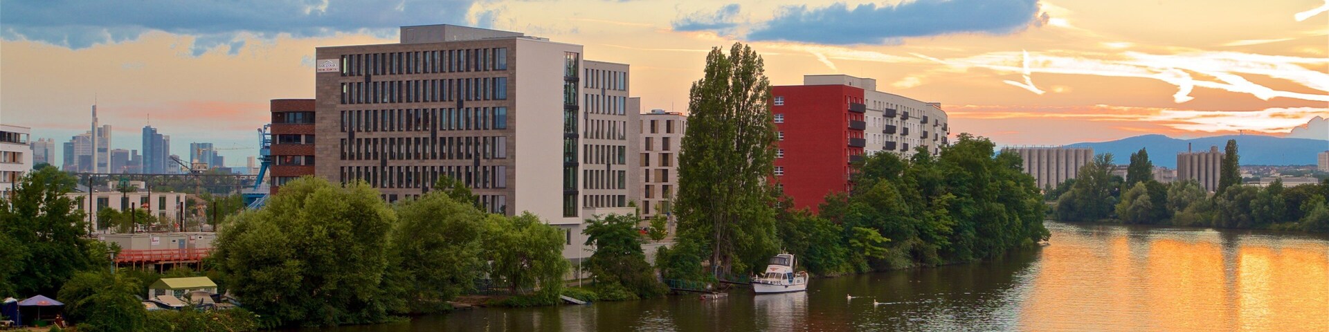Un río con una barca, rodeado de edificios modernos y árboles, durante el atardecer.
