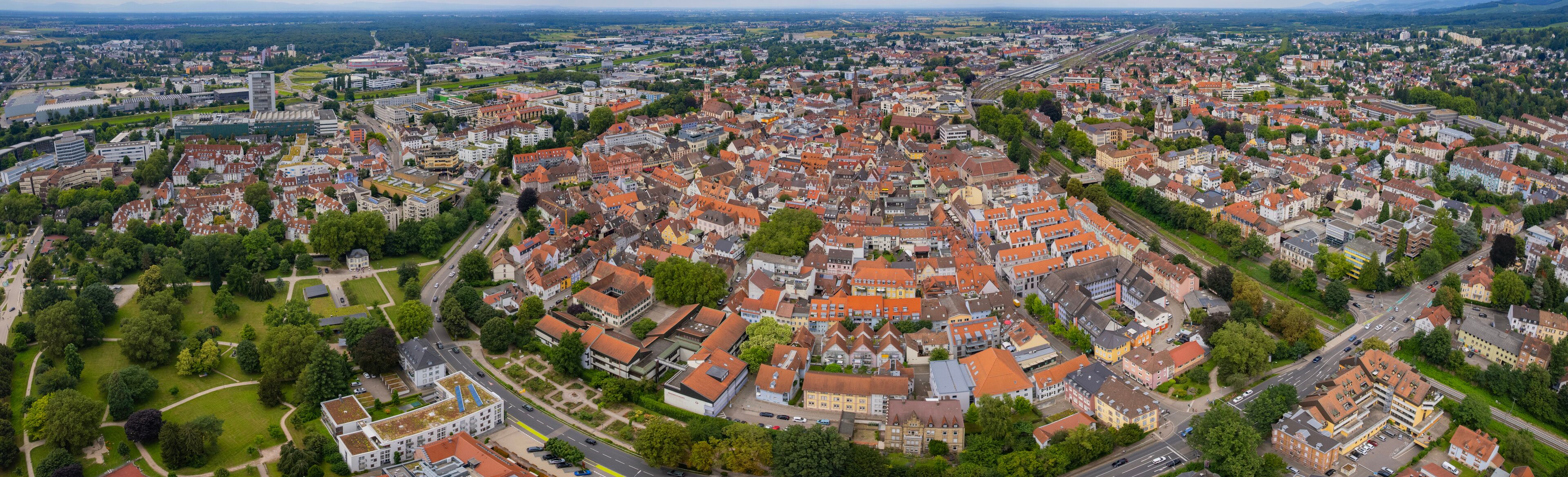 An aerial view of a densely built urban area with a mix of historic and modern architecture, surrounded by green spaces and roads.