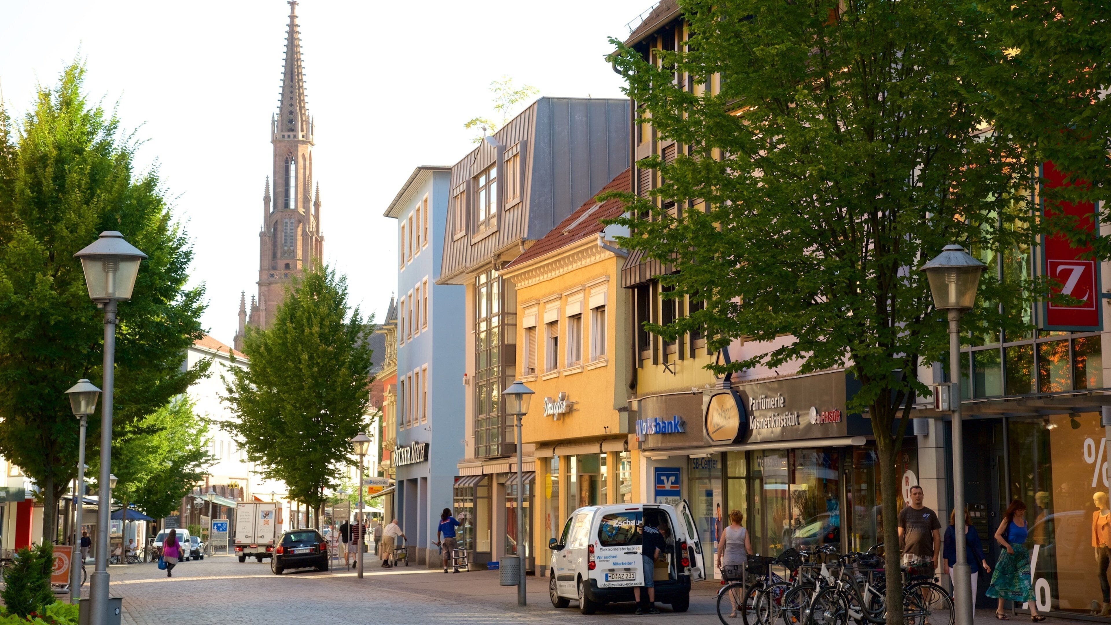 A cobblestone street lined with historic buildings, a church spire, and a modern shopping center.