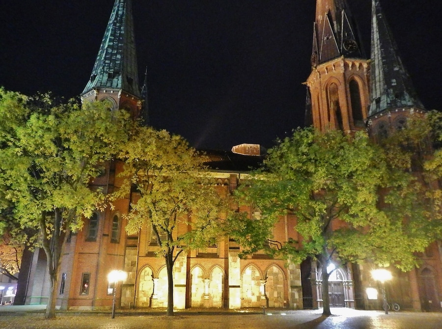 A historic building with two spires at night, illuminated by street lamps.