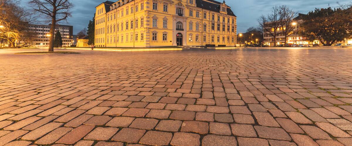 A historic building with a tower, a cobblestone plaza, and a clear sky.