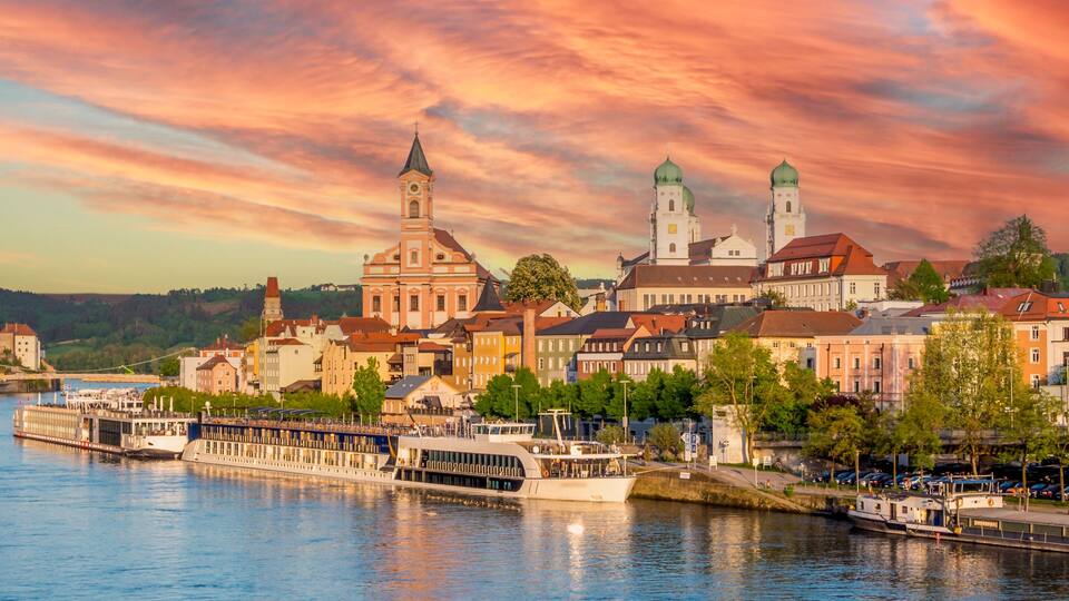 A river with boats, a bridge, and a town with colorful buildings and a church with two towers.