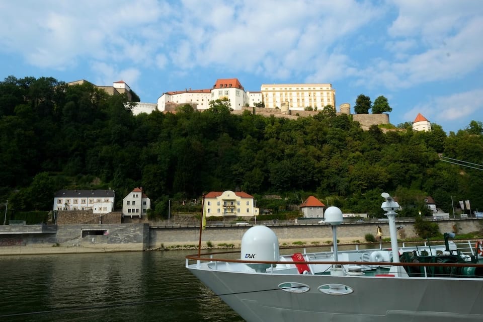 A boat docked near a river with a castle on a hill in the background.