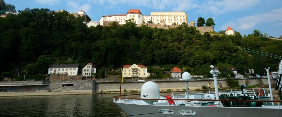 A boat docked near a river with a castle on a hill in the background.