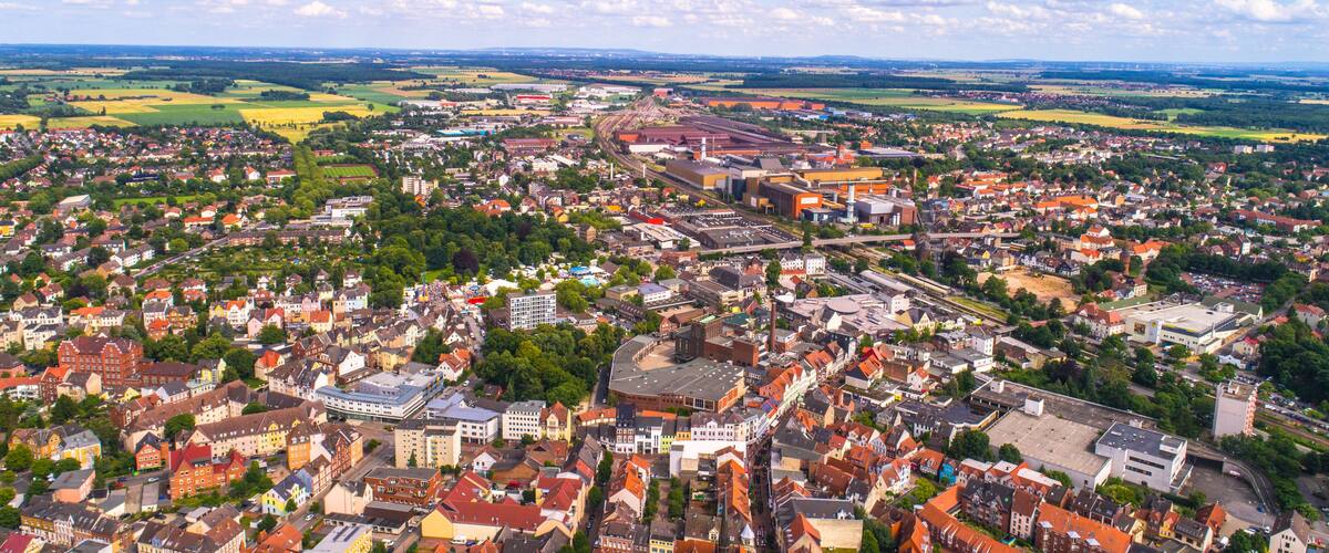 A panoramic view of a European town with a mix of historic and modern architecture, surrounded by green fields and a railway line.