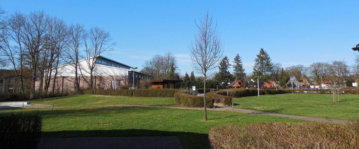 A park with a modern building, trees, and a clear blue sky.